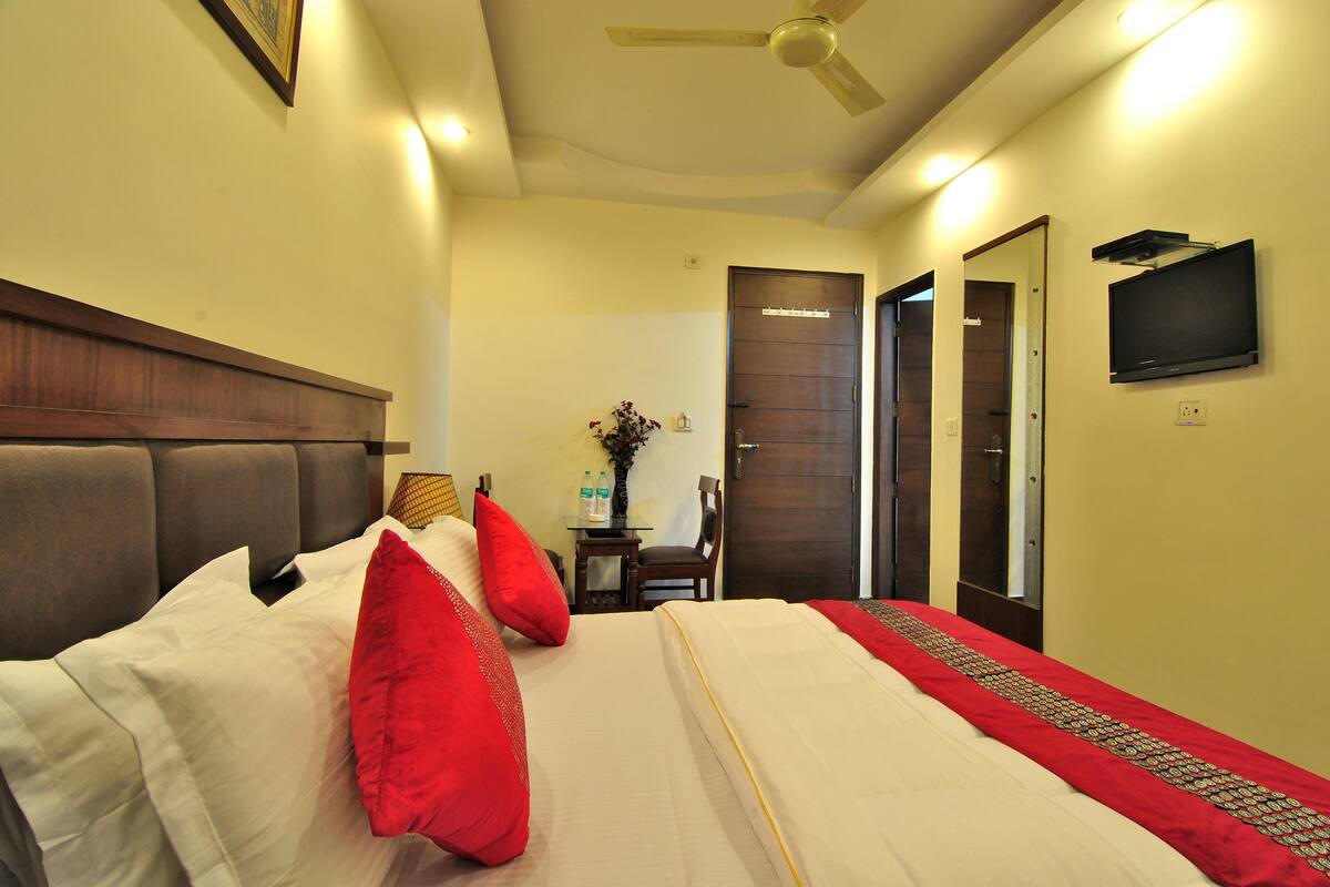 A hotel room with a bed, a ceiling fan, a television, and a door.