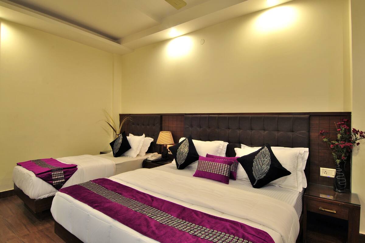 A hotel room with two beds, a nightstand, a lamp, and a vase with flowers.