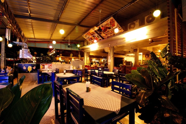 Un restaurante con mesas y sillas, un tablero de menú y plantas.