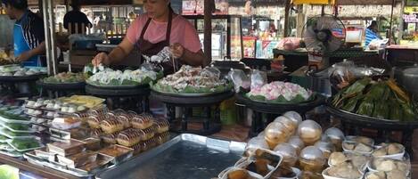 A food stall with various dishes displayed on trays and in containers.
