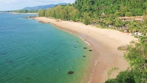 A beach with clear turquoise water, sandy shore, and lush green hills in the background. - Seabox Khaolak Hostel (Takua Pa)