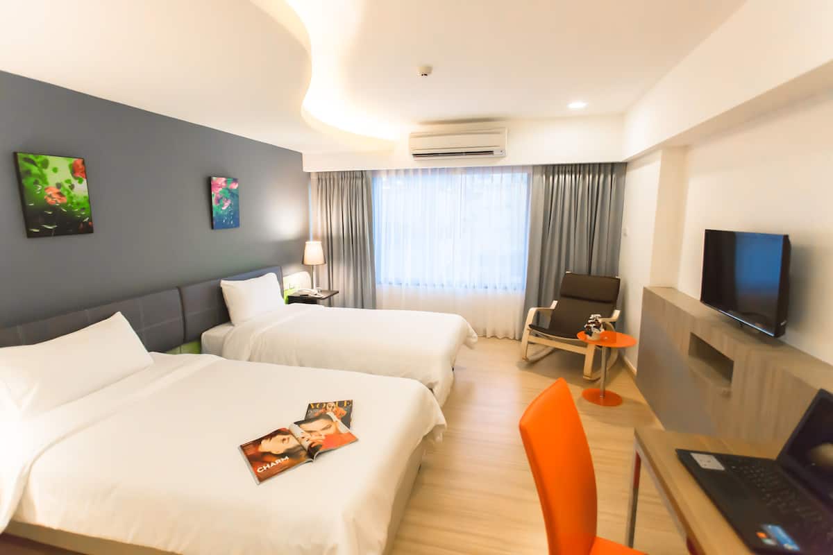 Quarto de hotel com duas camas, uma mesa com um laptop, uma televisão e uma cadeira.