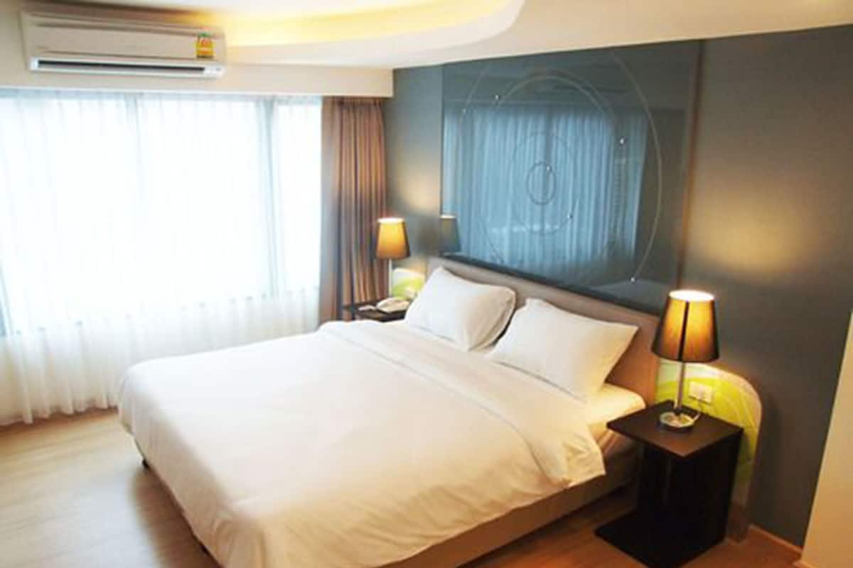 Quarto de hotel com uma cama grande, duas mesas de cabeceira com abajures, ar condicionado fixado na parede e uma janela com cortinas.