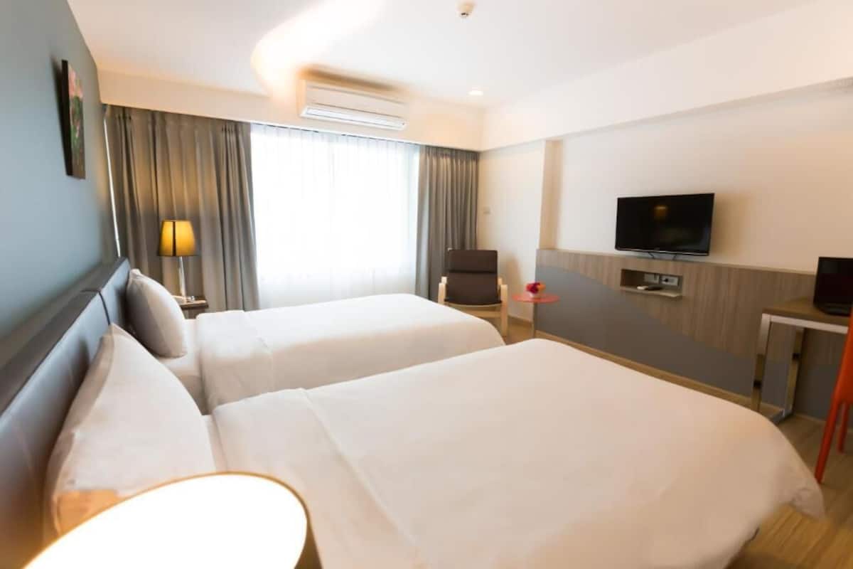 Quarto de hotel com duas camas, uma televisão, uma escrivaninha e uma cadeira.