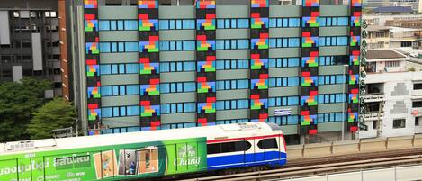 A train with colorful advertisements on a track, passing by a building with a patterned facade.