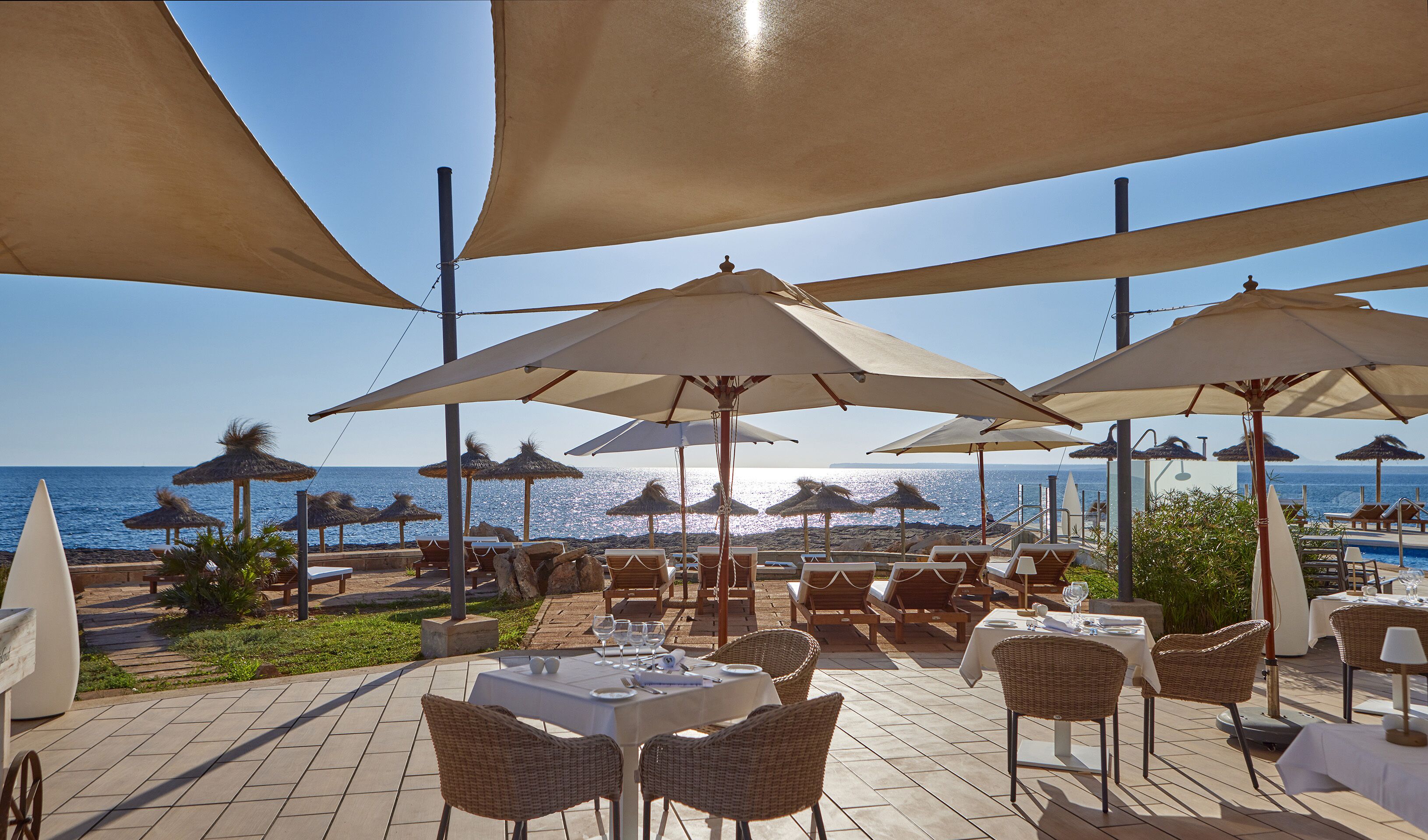 An outdoor dining area with tables and chairs, umbrellas, and a view of the sea.