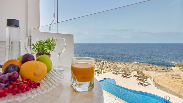 A table with fruits, a glass of juice, and a potted plant by a poolside with a view of the sea. - Universal Hotel Cabo Blanco - Adults Only (Ses Salines)