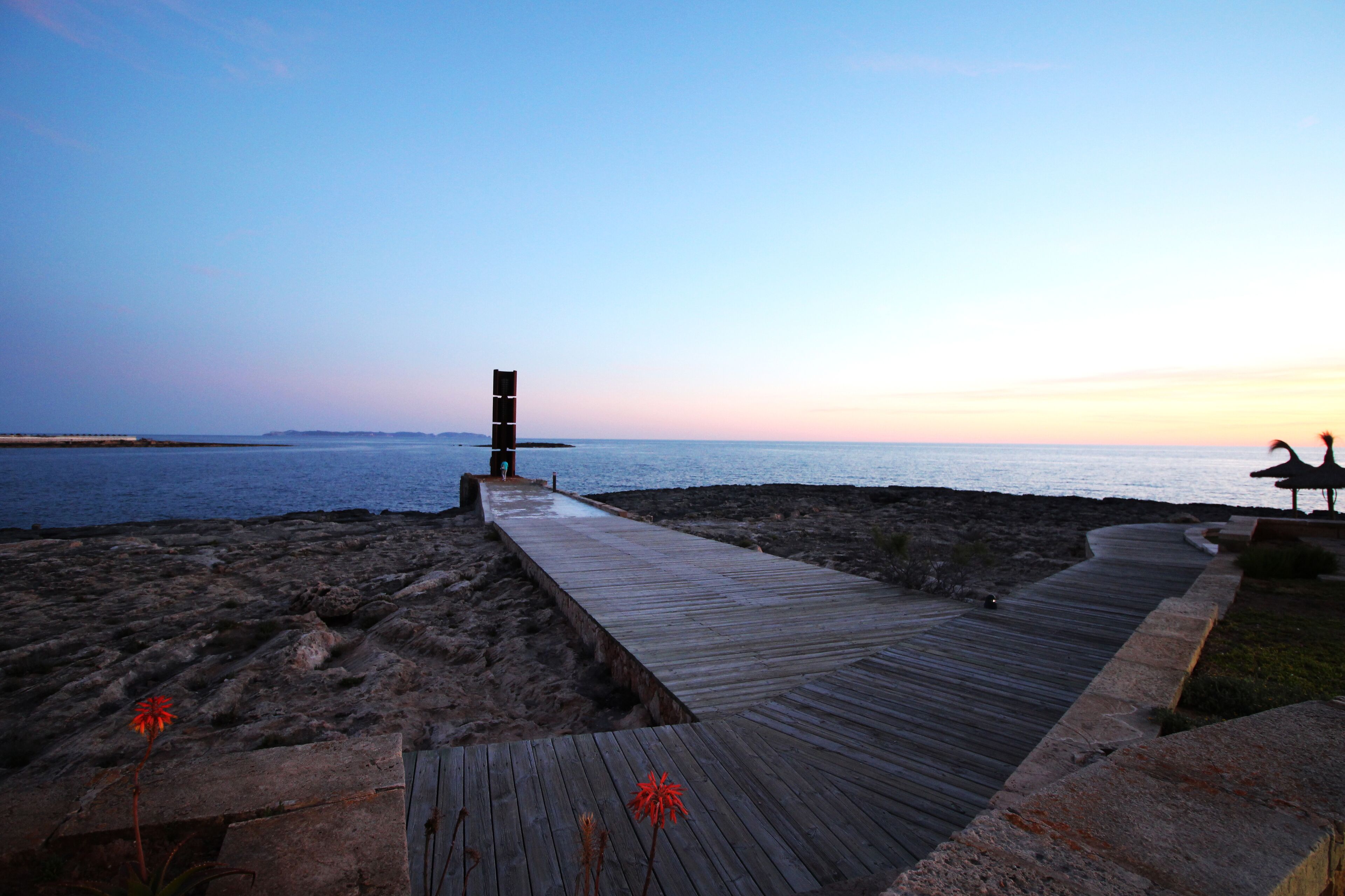 Un malecón de madera que conduce a una playa con una pila de sillas y una escultura de pájaro.