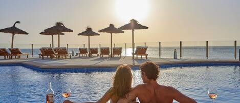 A couple relaxing by a poolside with a sunset view, lounge chairs, and umbrellas.