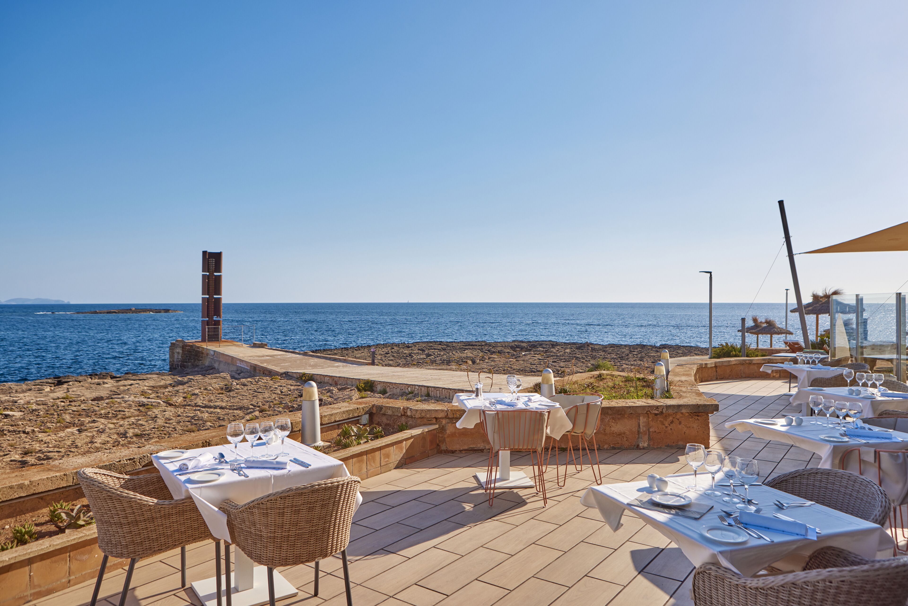 An outdoor dining area with tables and chairs, overlooking the sea.