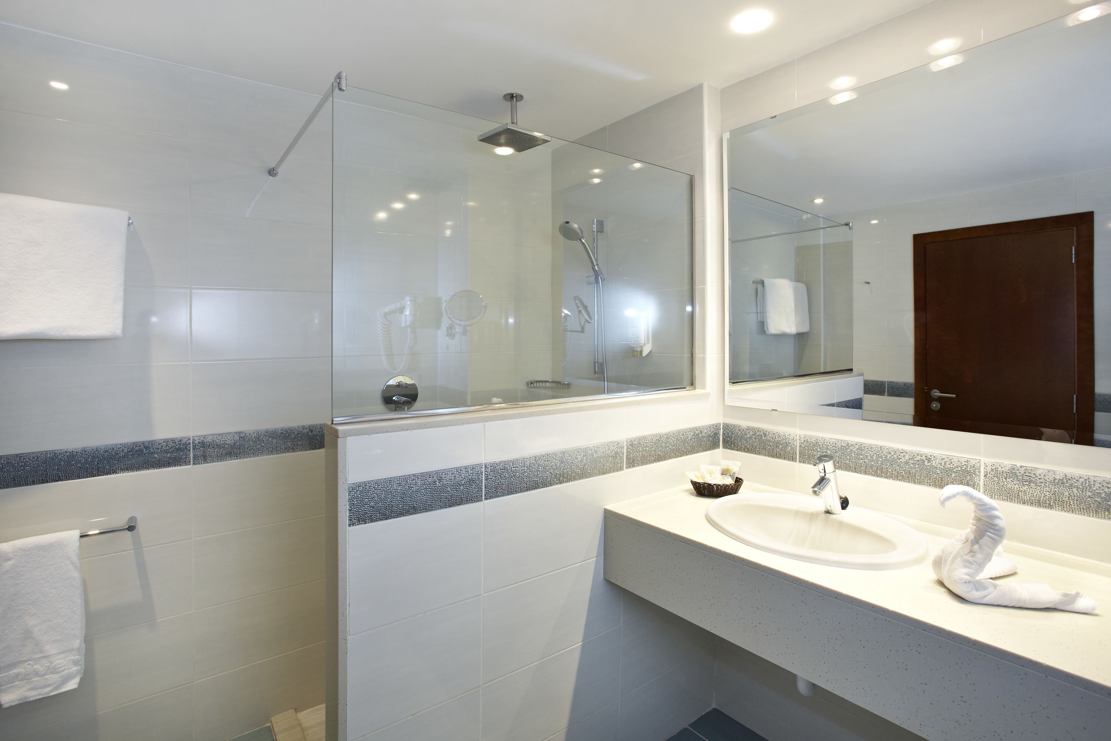 A modern bathroom with a glass-enclosed shower, a large mirror, and a white sink with a swan-shaped soap holder.