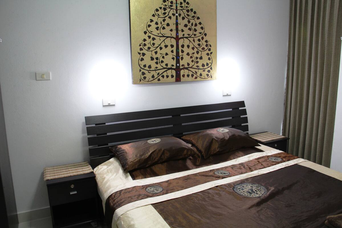 A neatly made bed with a patterned bedspread, two bedside tables, and a wall-mounted light fixture.