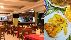 Ein Restaurantinneres mit Holztischen und -stühlen, einer Bar und einem an der Wand befestigten Fernseher.