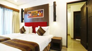 Habitación de hotel con una cama grande, una mesita de noche pequeña, un televisor montado en la pared y una puerta que da a otra habitación.