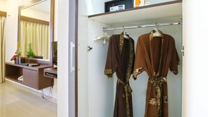 A hotel room with a large mirror, a vanity with a sink, a robe rack with two robes, and a shelf with a radio and decorative items. - The Swaha Ubud Hotel (Batubulan)