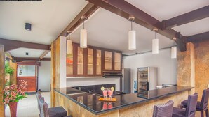 A modern kitchen with a central island, bar seating, and hanging pendant lights. - The Swaha Ubud Hotel (Batubulan)