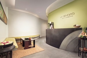Een receptiezone met een gebogen wand, een receptiebalie en een zithoek met een bank en tafels.
