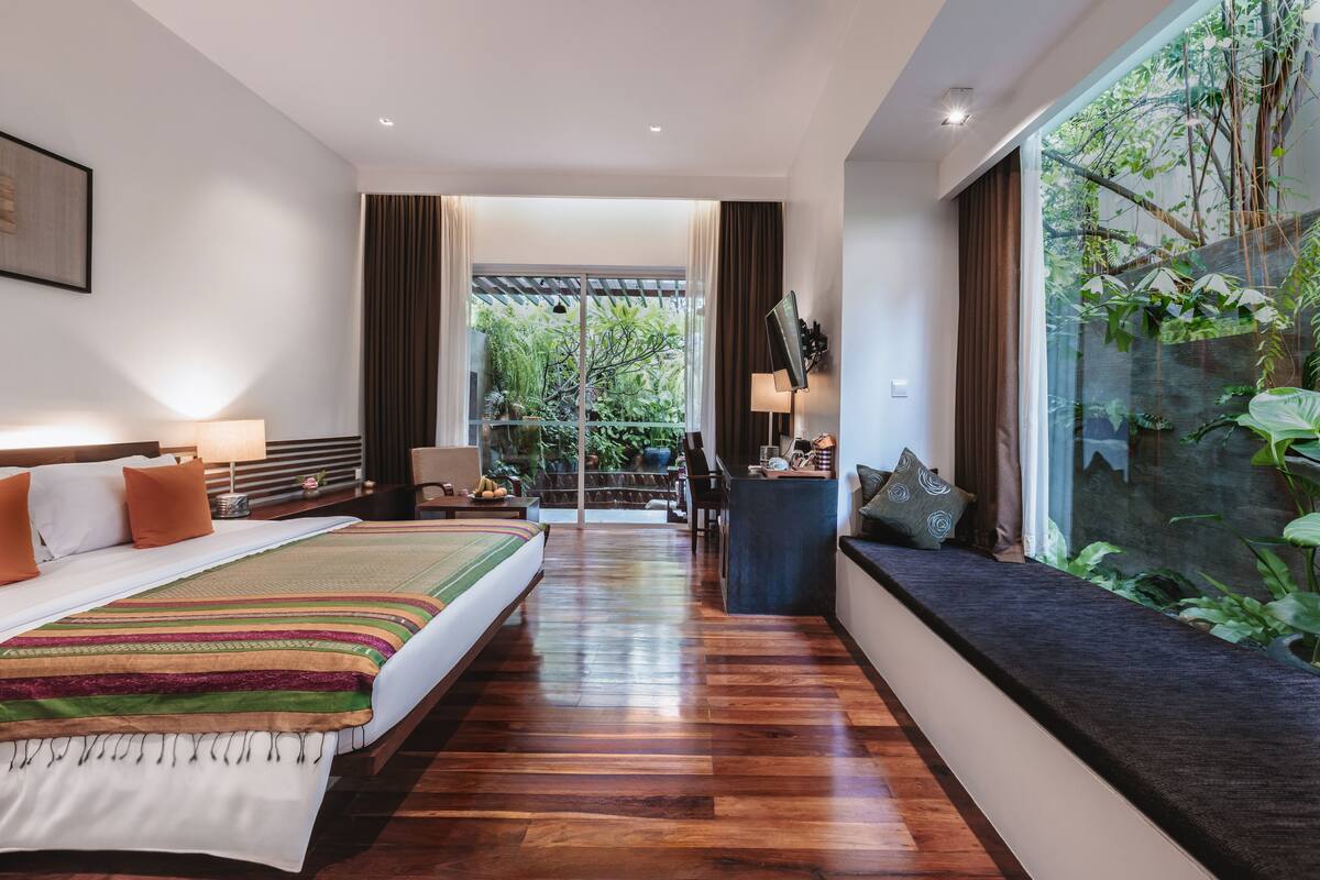 Une chambre d’hôtel moderne dotée d’un grand lit, d’un coin salon avec vue et d’un balcon agrémenté de plantes.