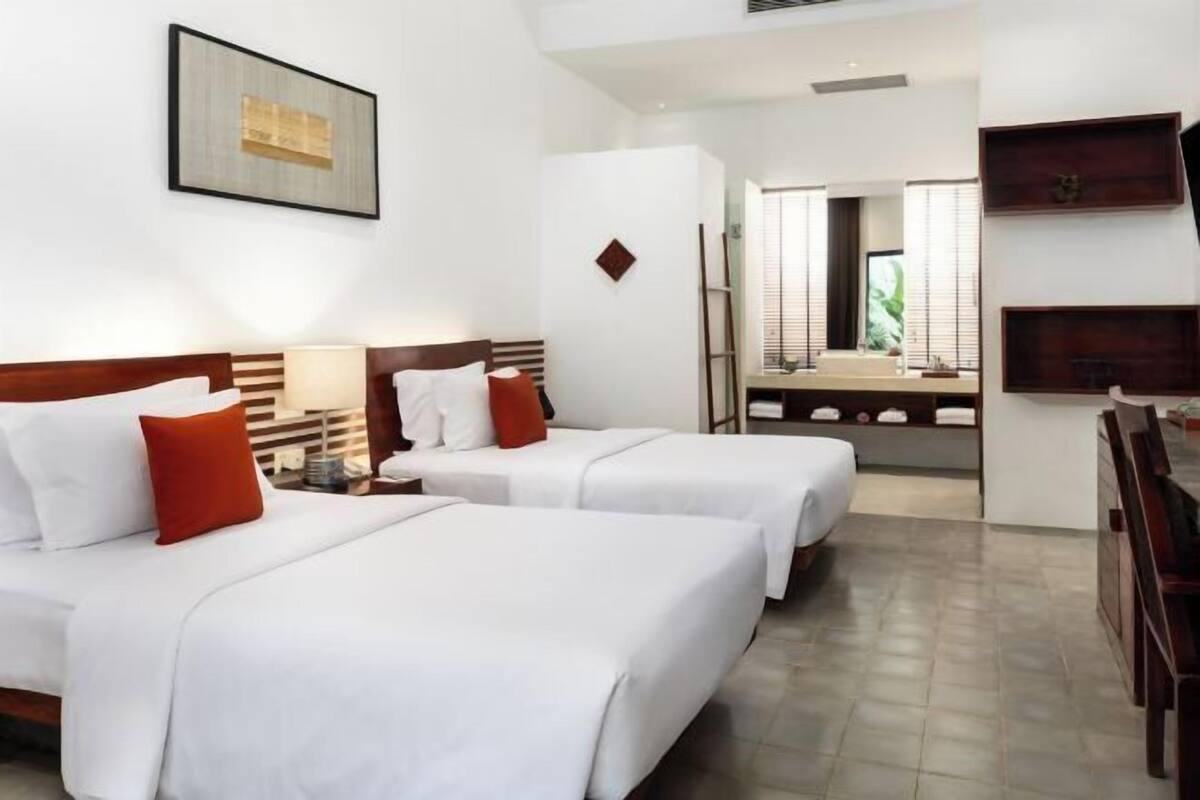 Une chambre d’hôtel avec deux lits, une salle de bain avec un miroir et un bureau avec une chaise.