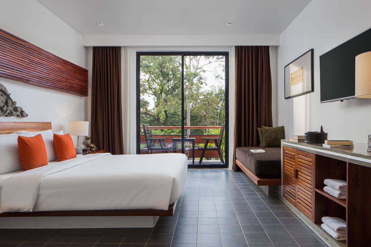 Une chambre d’hôtel moderne avec un grand lit, un bureau et un balcon donnant sur la verdure.