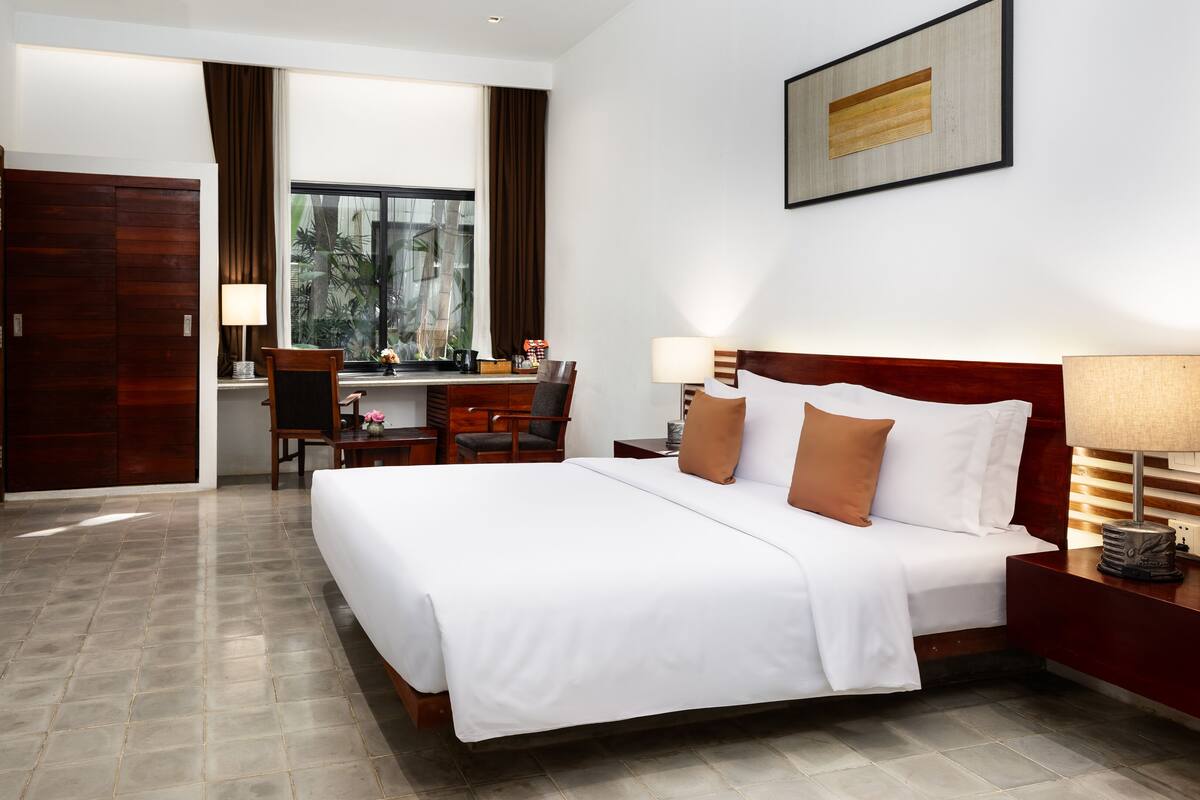 Une chambre d’hôtel avec un grand lit, un bureau, une chaise, une télévision et une fenêtre avec des rideaux.