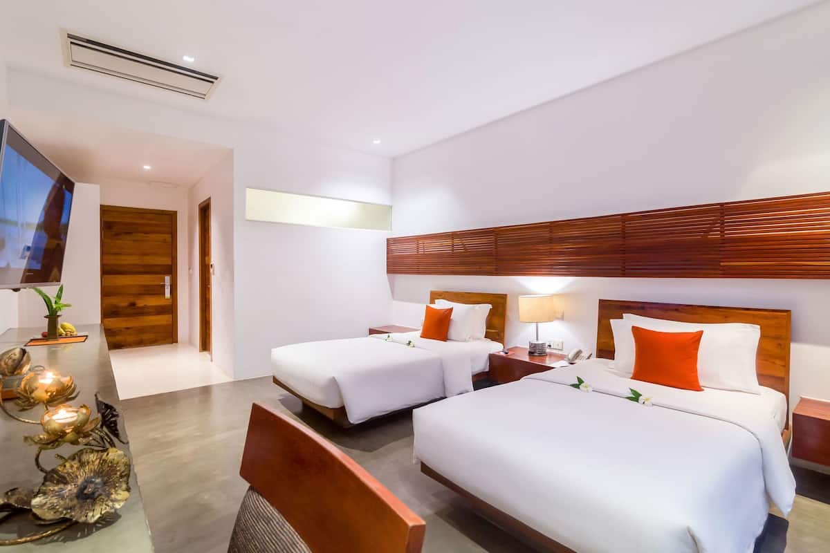 Une chambre d’hôtel avec deux lits, une télévision, une tête de lit en bois et une plante.