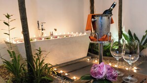 Ein ruhiger Innenraum mit einem kerzenbeleuchteten Weg, einem Metallkübel mit einer Flasche und zwei leeren Weingläsern auf einem Holztisch.
