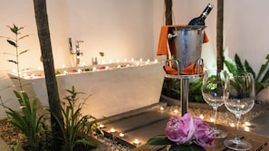 Een rustgevende binnenruimte met een kaarsverlicht pad, een metalen emmer met een fles en twee lege wijnglazen op een houten tafel.