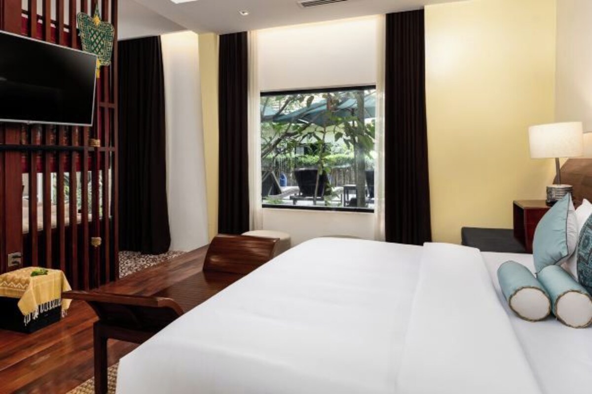 Hotelkamer met een bed, televisie, bureau, stoel, raam met uitzicht op groen en nachtkastje met lamp.