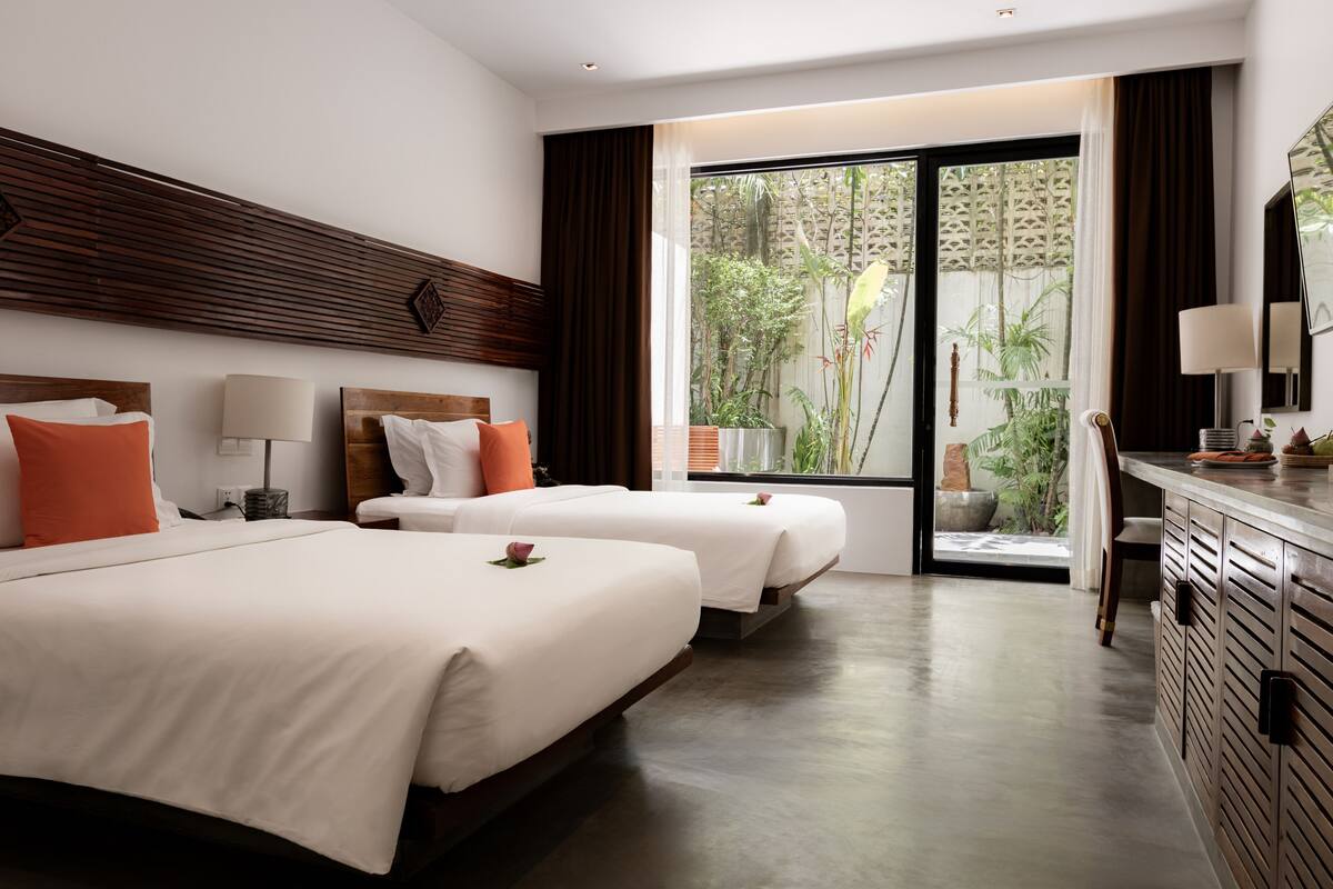 Une chambre d’hôtel avec deux lits, un bureau et une vue sur la verdure environnante.