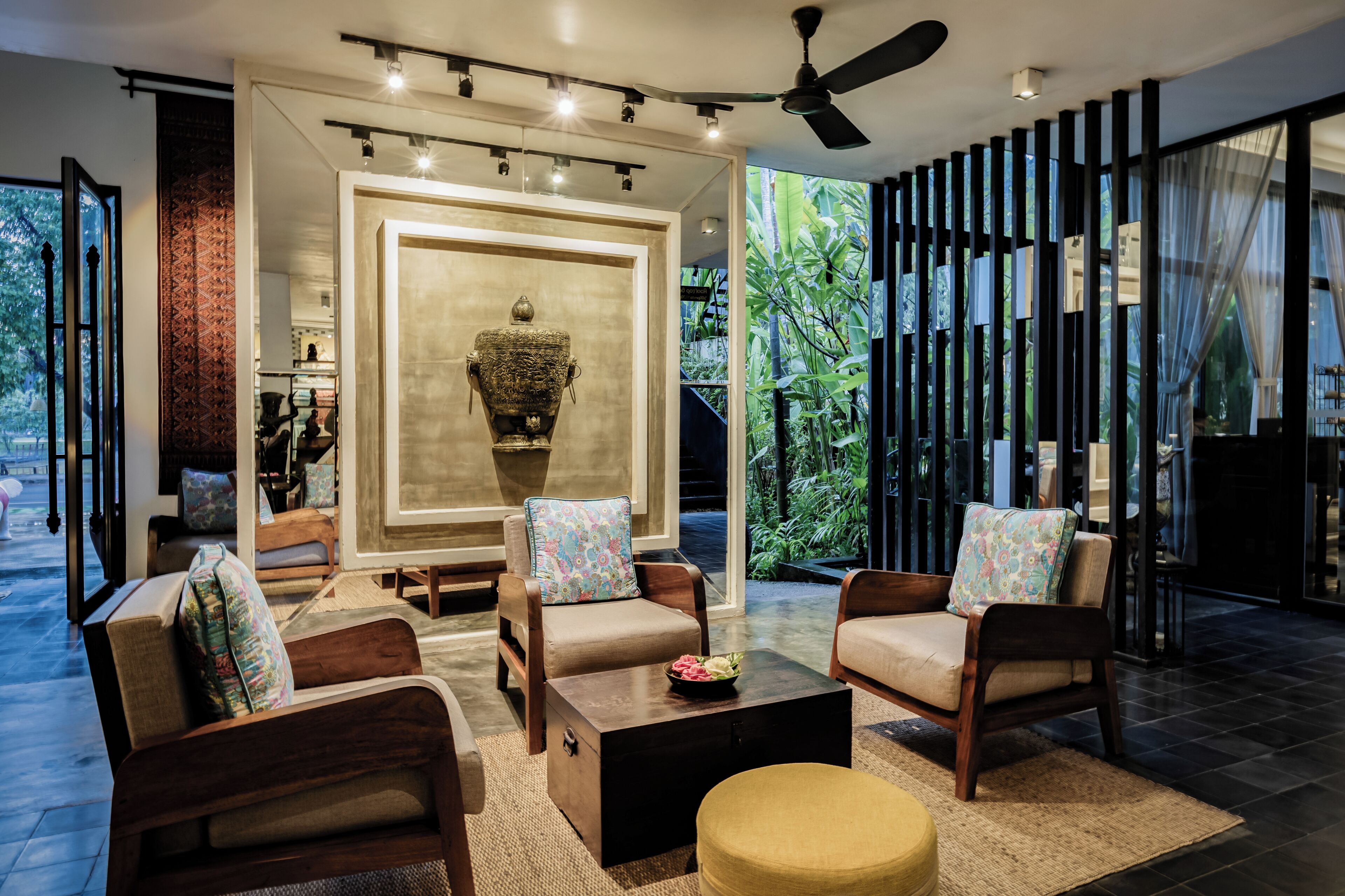 A modern living room with a large decorative urn, comfortable seating, and a view of greenery through large windows.
