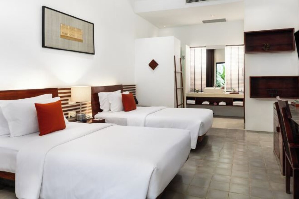 Une chambre d’hôtel avec deux lits, une salle de bain avec un miroir et un bureau avec une chaise.