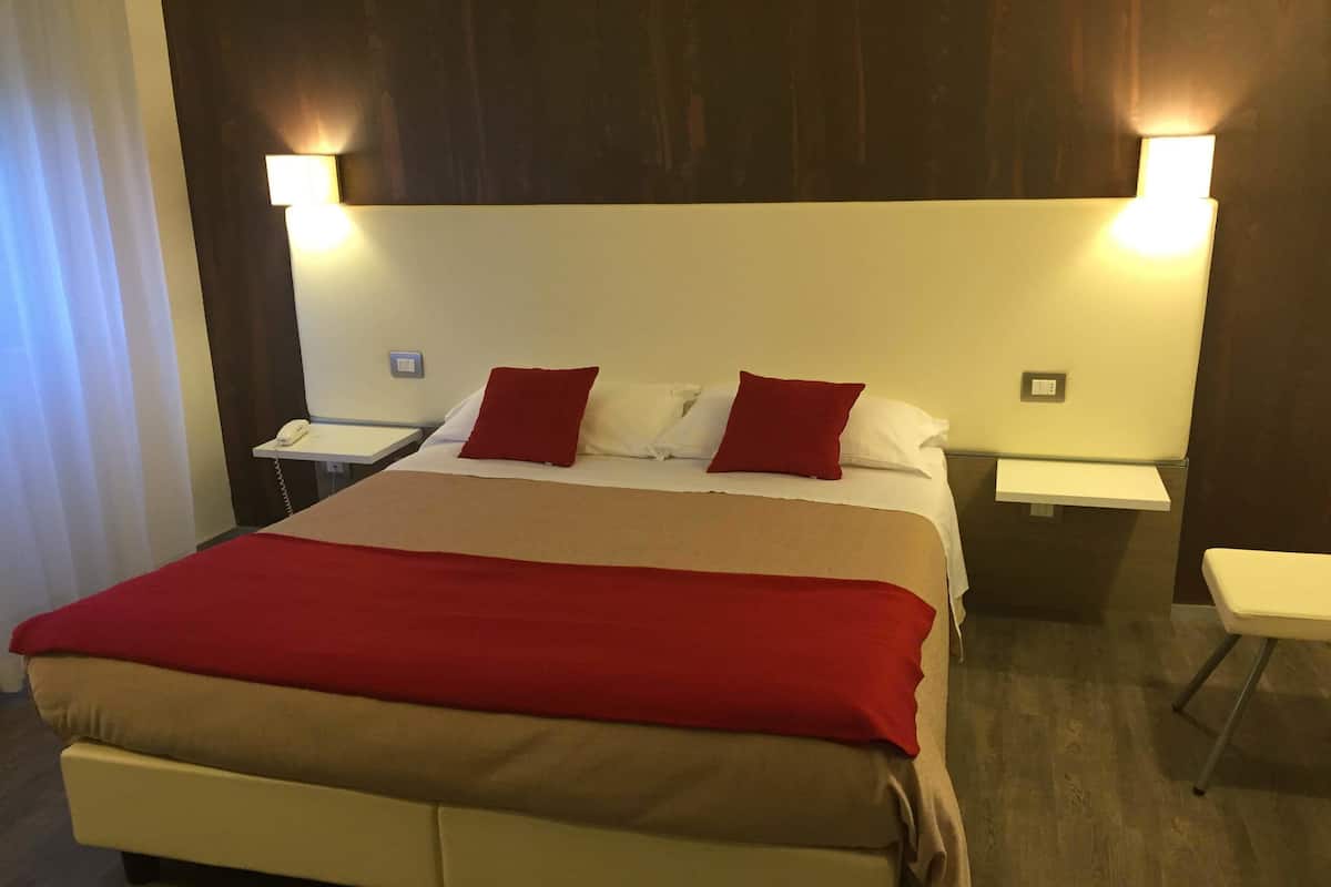 Een hotelkamer met een groot bed, twee nachtkastjes en een stoel.