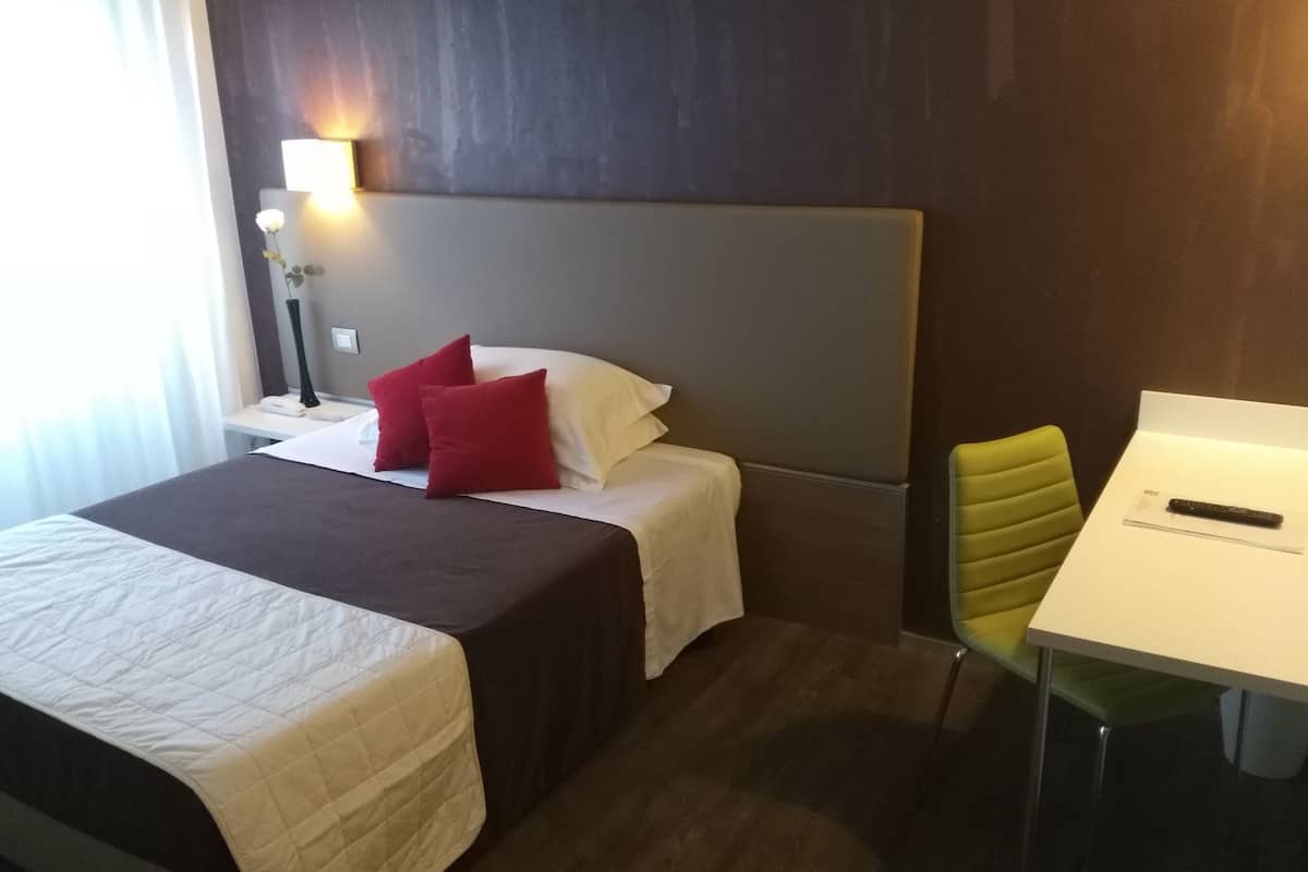 Een hotelkamer met een bed, nachtkastje, lamp en een bureau met stoel.