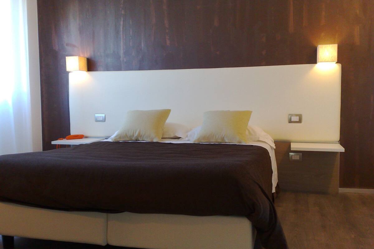 Een moderne hotelkamer met een groot bed, twee bedlampen en een donker houten hoofdeinde.