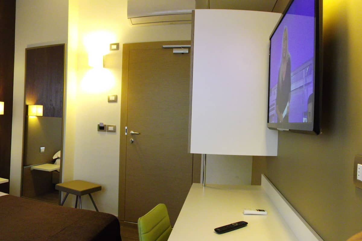 Een hotelkamer met een bed, nachtkastjes, een bureau, een stoel, een televisie en een spiegel.