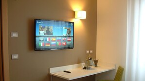 Une chambre d’hôtel équipée d’un téléviseur fixé au mur, affichant une interface Smart TV, d’un petit bureau avec une chaise et d’une bouteille de champagne posée sur la table.