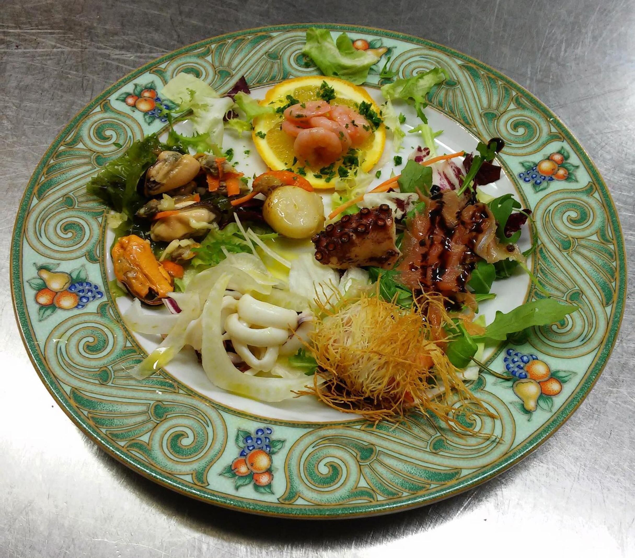 A plate with a variety of seafood and vegetables, including octopus, mussels, and lemon slices, on a decorative ceramic plate.