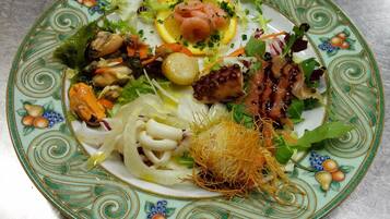 A plate with a variety of seafood and vegetables, including octopus, mussels, and lemon slices, on a decorative ceramic plate.