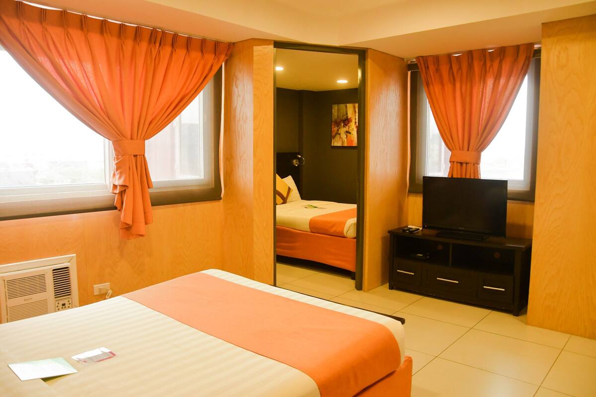 A hotel room with a bed, a TV, and a bathroom visible through an open door.