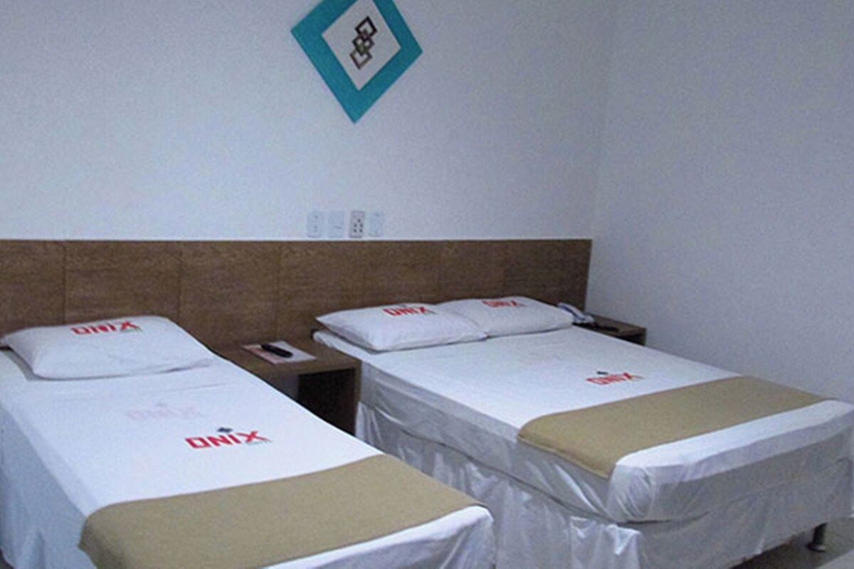 Une chambre d’hôtel avec deux lits, chacun recouvert d’une courtepointe blanche et d’une couverture marron. Il y a une table de chevet avec un téléphone et une petite table entre les deux lits.