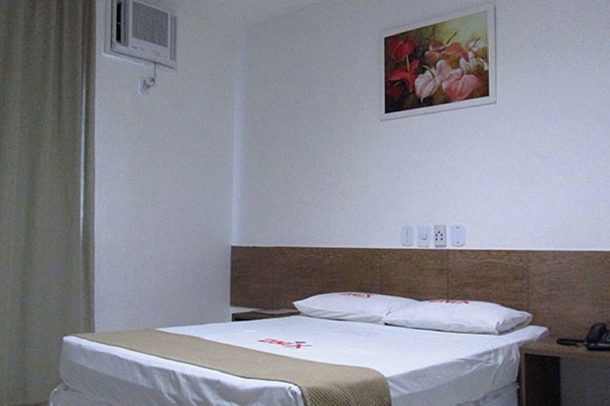 Een hotelkamer met een bed, een nachtkastje met een telefoon en een schilderij aan de muur.