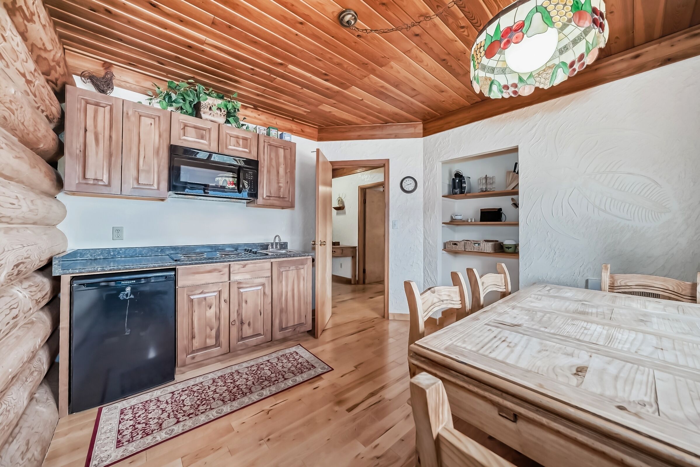 A log cabin interior with wooden cabinets, a kitchen area, a dining table, and a ceiling light fixture.