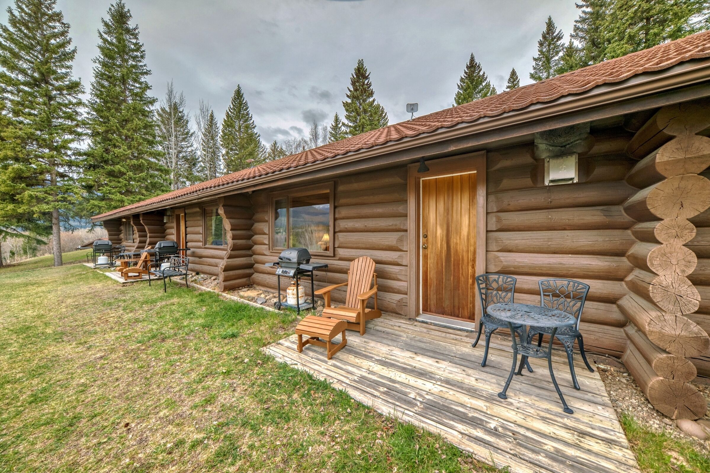 A log cabin with a porch, outdoor seating, and a grill.