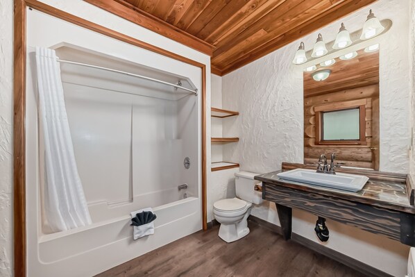 A bathroom with a bathtub, toilet, and vanity with a sink and mirror. - Terracana Ranch Resort (Valemount)