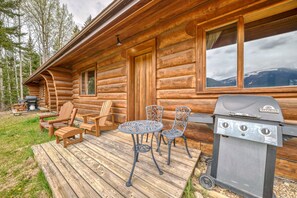 A log cabin with a deck, outdoor seating, and a grill.