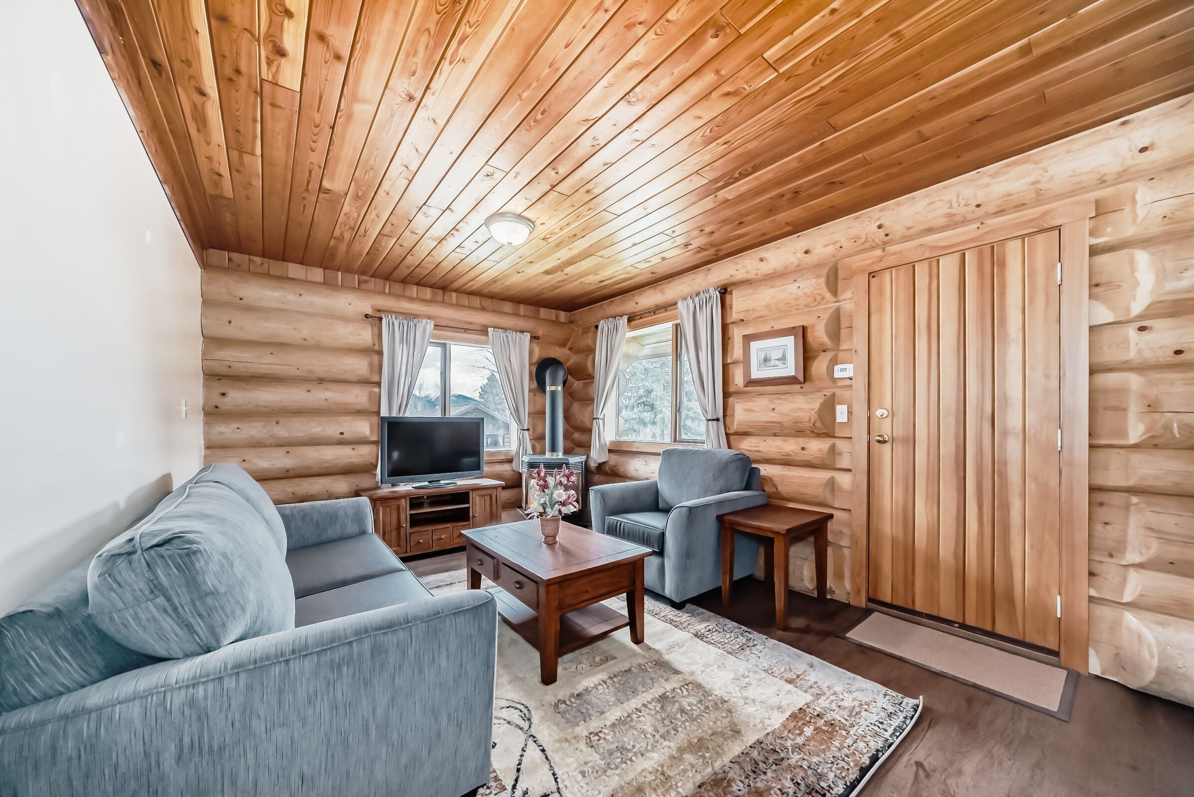 Ein Holzblockhaus-Interieur mit einer Couch, einem Sessel, einem Fernseher und Holzwänden.