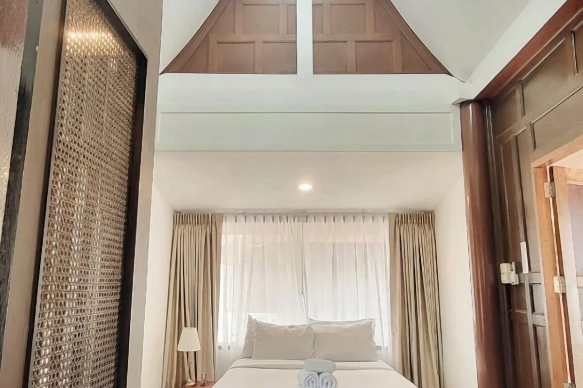 Habitación de hotel con cama, cortinas, una lámpara y pared texturizada.