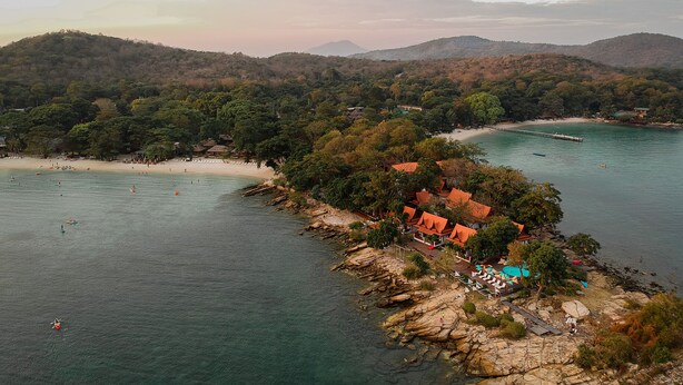 Eine Küstenlandschaft mit Strand, felsigem Ufer und einem Gebäude mit rotem Dach.