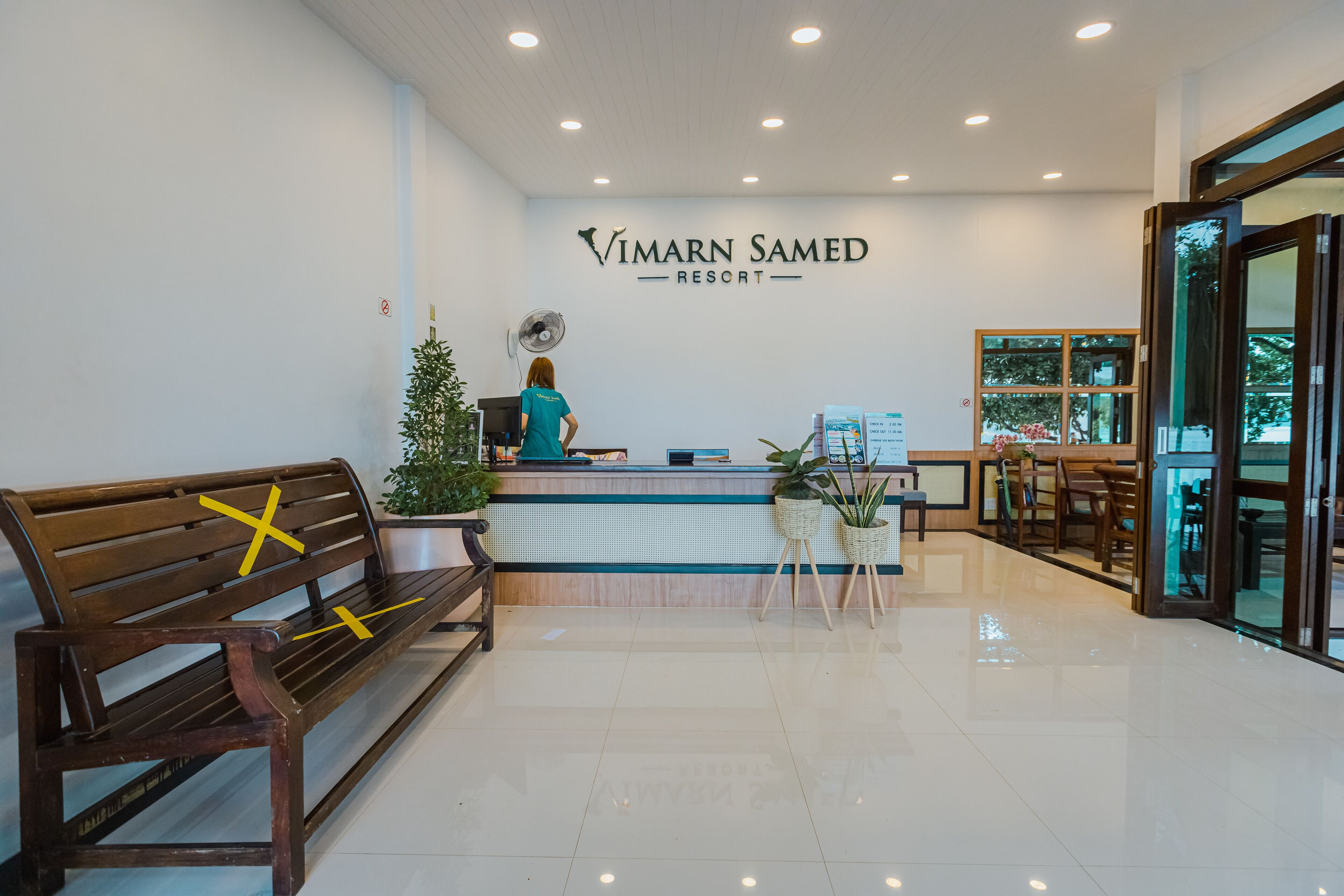 Un área de recepción con un banco de madera, mostrador y plantas en macetas.
